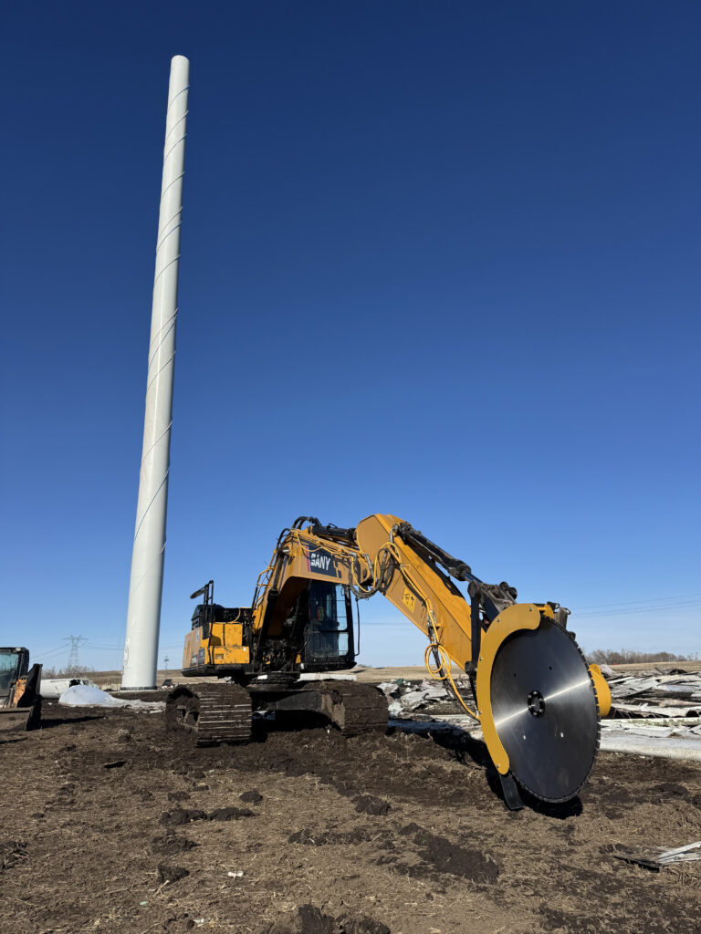Excavator with saw mount decommissioning wind turbine.